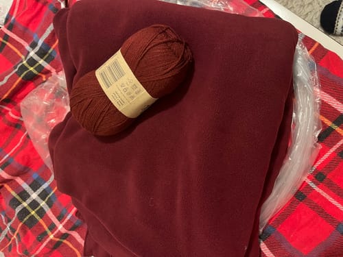 Close-up of a reviewer's wine-colored polar fleece fabric, folded with a matching ball of yarn on top.