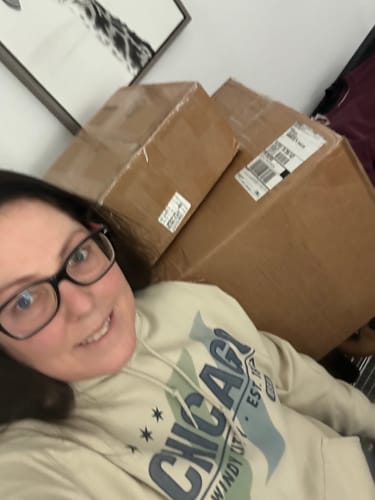 Customer wearing a hoodie from their Wholesale Branded Sweatshirts order, sitting in front of the large shipping boxes.