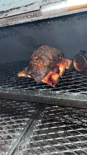 Customer's Bone-In Short Ribs with a dark, rich crust cooking inside a smoker.