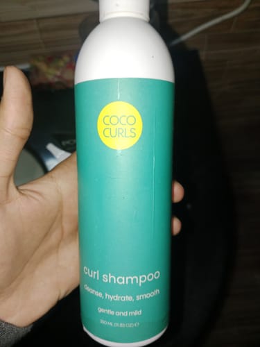 Reviewer holding the teal bottle of Coco Curls Curl Shampoo.