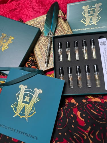 Reviewer's open Discovery Set showing numerous perfume vials arranged with its elegant packaging and a quill pen.