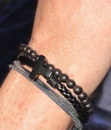 Close-up of a reviewer's wrist wearing several black bracelets with a cross, showing support for veterans.