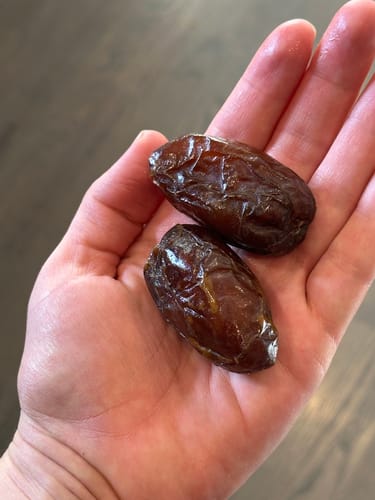 Reviewer holding two plump, juicy Organic Rutab Medjool Dates in the palm of their hand.