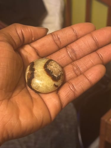 Customer holding a polished, round monthly crystal with brown swirls in their palm.