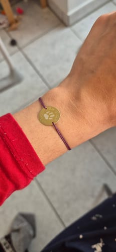 Ein Rezensent trägt das Armband „Pfotenabdruck“ mit goldenem Anhänger und violettem Band am Handgelenk.