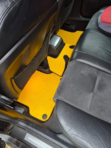 Recenzent pokazuje jaskrawożółte dywaniki samochodowe, idealnie dopasowane do podłogi na tylnych siedzeniach auta.