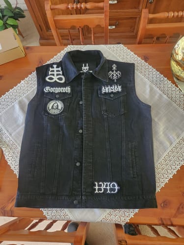 Customer's black The Left Hand Black - Vest with several custom patches added, laid flat on a table.