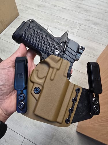Customer holding a tan T1-ECHO holster with a handgun inserted, showing its dual black clips and flexible center.