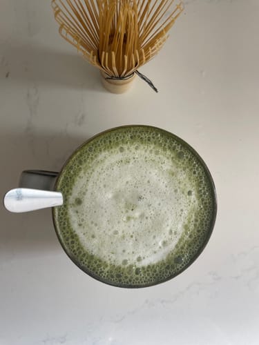 Un cliente muestra su té matcha espumoso del Pack Experiencia Iniciación con el batidor de bambú al fondo.