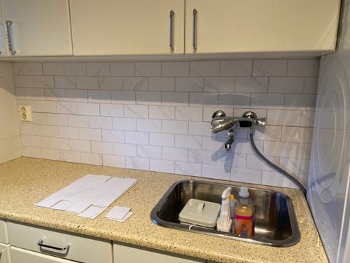 Kundens Stein subway marmor veggfliser installert på en kjøkkenvegg over en vask, med tilpasninger rundt kranen.