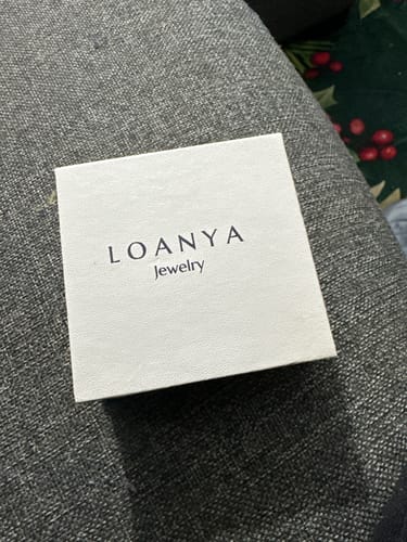 Rezensent zeigt die weiße Schmuckschachtel für das Herringbone Armband auf einer Couch.