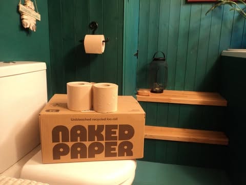 Customer's unbleached recycled toilet paper rolls and branded box displayed on a toilet in a green bathroom.