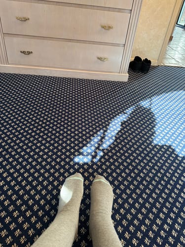 Reviewer's first-person view of their feet in tan Premium Bamboo Compression Socks on a patterned carpet.
