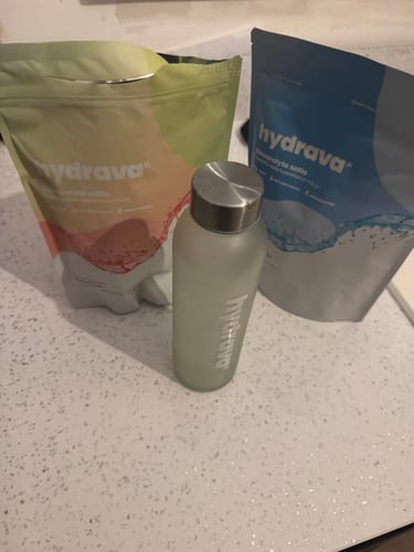 Reviewer's two different pouches of hydrava electrolyte salts next to a branded water bottle on a countertop.
