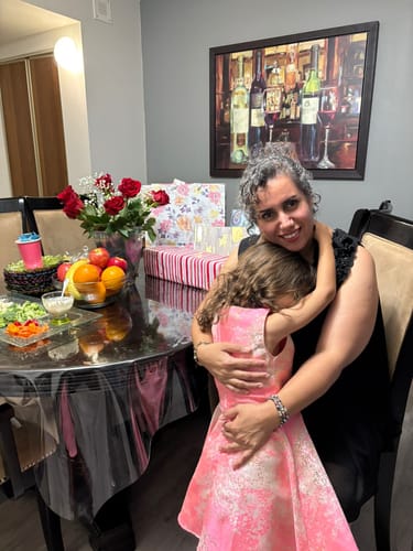 Reviewer with beautiful, silver-toned curly hair smiling while hugging a child at a celebration.