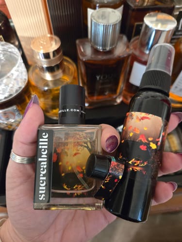 Customer holding Cauldron Eau de Parfum and body mist bottles in front of their fragrance collection.