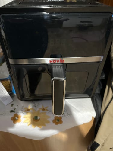 Clientul arată friteuza sa neagră cu aer cald Novio StonePro pe o masă acoperită cu o față de masă.