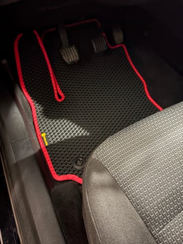 Klient pokazuje czarny dywanik samochodowy z czerwonym obszyciem, idealnie dopasowany w miejscu kierowcy.