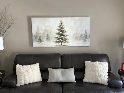 Customer's canvas painting of a snowy forest displayed over a dark sofa in their living room.