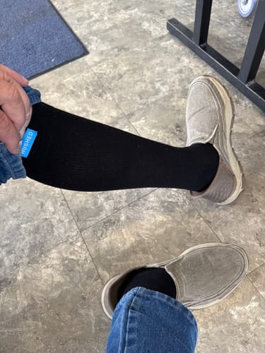 Customer seated, pulling up a pant leg to show the black Performance Eucalyptus Compression Sock on their leg.