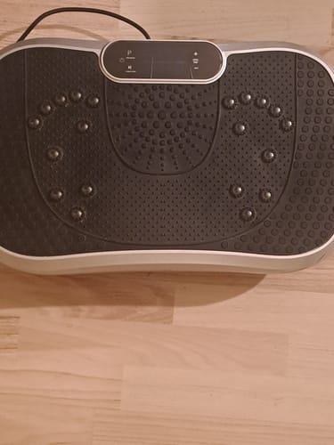Anmelderens grå vibrationstræner med sort akupressur-top, set fra oven på et trægulv.