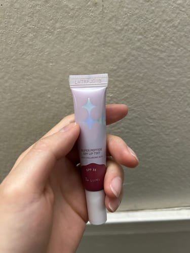 Customer holding the purple and clear tube of Super Peptide SPF Lip Tint in their hand.