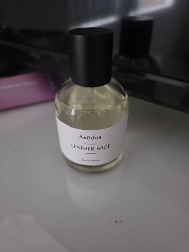 Customer's bottle of LEATHER SAGE EAU DE PARFUM with a black cap, sitting on a table.