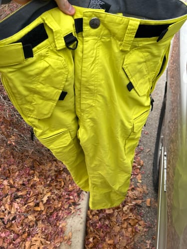 Customer holding up the baggy, fluorescent yellow snow pants, showing the adjustable waistband and pockets.