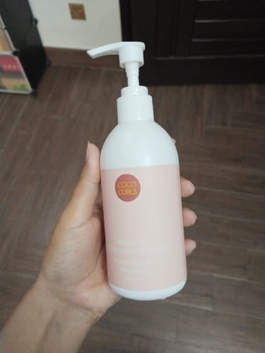 Customer holding the white pump bottle of Leave-in Glossy Conditioner indoors.