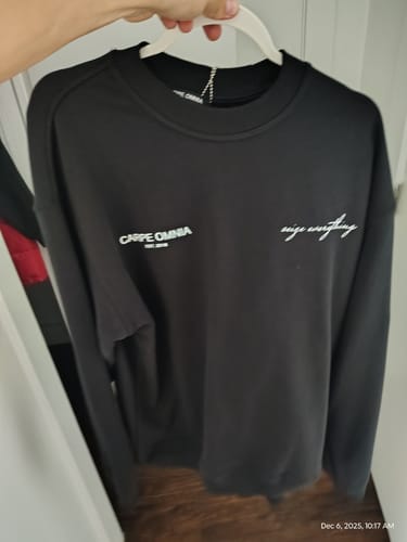 Reviewer holding up their black Definition 2.0 Sweatshirt on a hanger, showing the white logos on the front.