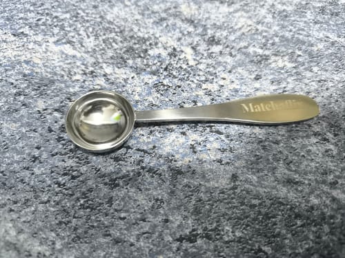 Un cliente muestra la Cuchara Medidora de Acero Inoxidable sobre una superficie gris texturizada.