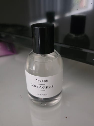 Customer's bottle of 300 Oakmoss Eau De Parfum in a simple glass bottle with a black cap on a table.