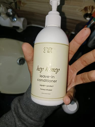 Customer holding the white pump bottle of Hey Honey Leave-in Conditioner in their hand.