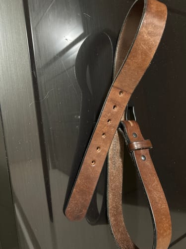 Reviewer's well-worn brown leather The Everyday belt coiled on a dark surface, showing its durability.
