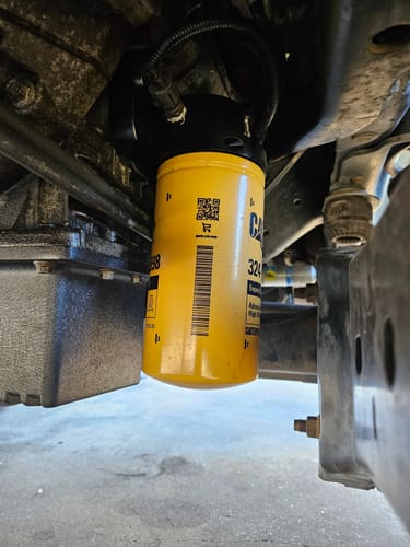 Customer's installed SPE Motorsport Oil Filter Housing with a yellow CAT filter shown underneath a Ford Powerstroke.