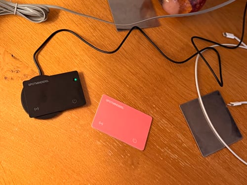 Customer's black and pink SPOTMINDERS tracking cards on a wooden desk. One card is charging wirelessly with a green light.