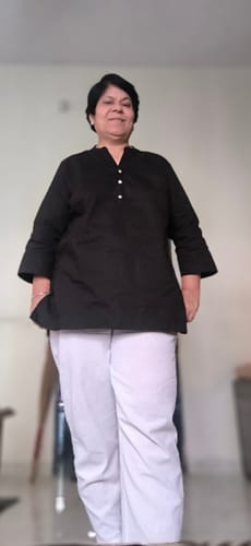 Reviewer standing indoors wearing the black airy linen short kurta with white trousers, showing the simple fit.