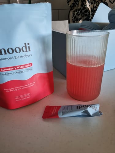Reviewer's Electrolytes 10Pk pouch and an empty sachet next to a glass of the prepared red drink.