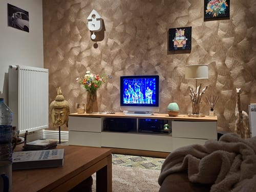 Recensentfoto van de witte Karlsson Wandklok Cuckoo die aan een gestructureerde muur in een woonkamer hangt.