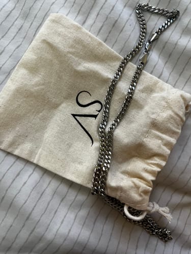 Cliente mostrando su Cadena Miami Cuban de 5mm plateada, sobre su bolsa de tela con el logo.
