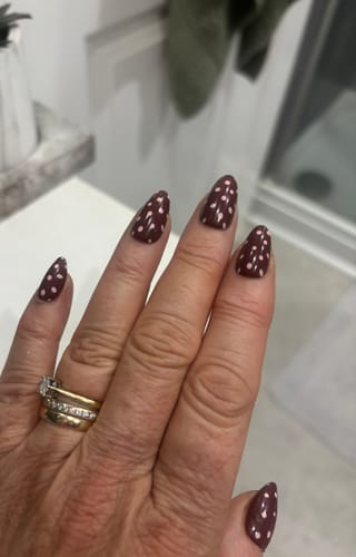 Customer's hand showing the applied Spot On press-on nails, which are dark brown with pink polka dots.