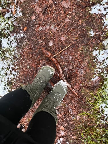 Asiakkaan vihreät Vaistoa Hanki 2 -saappaat seisomassa lumisella metsänpohjalla.