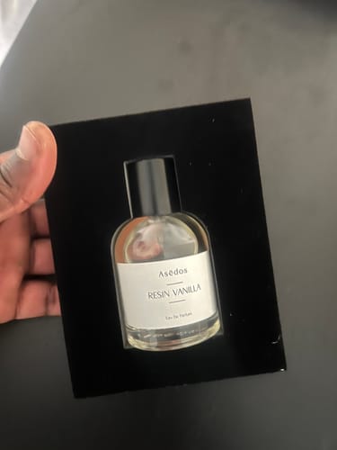 Reviewer holding the RESIN VANILLA EAU DE PARFUM bottle inside its black product holder.
