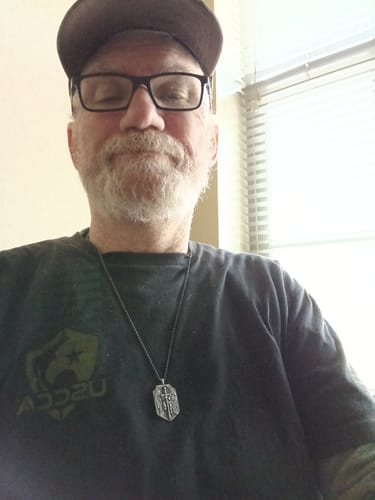 Reviewer, a veteran and supporter, shown in a selfie wearing a pendant necklace.