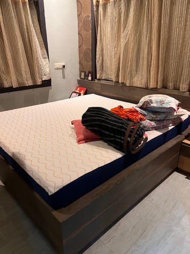 Customer's white and blue Flo Mattress Ortho placed on a dark wooden bed frame in a bedroom.