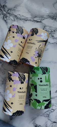 Cliente muestra tres botes de Té Matcha Vainilla Premium y otro bote de matcha sobre una superficie de mármol.