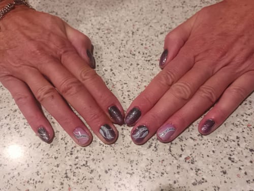 Hände einer Kundin mit einer Mix-and-Match-Maniküre, die die schimmernden Fuchsia Fade Cat Eye Nagelfolien mit Stickern kombiniert.