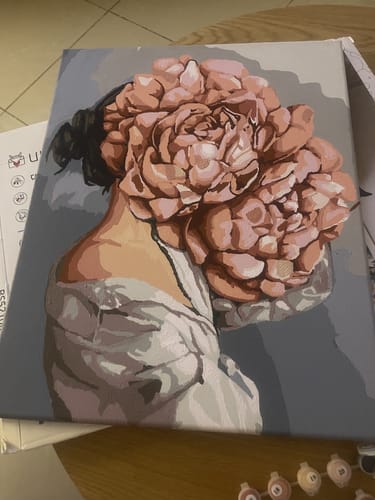 לקוחה מציגה את ציור הצביעה לפי מספרים שסיימה, המתאר דמות עם פרח ורוד גדול.