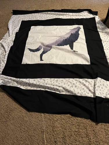 Reviewer's Misty Mountain Wolf Silhouette Fabric Panel sewn into a beautiful black and white quilt top spread on a carpet.