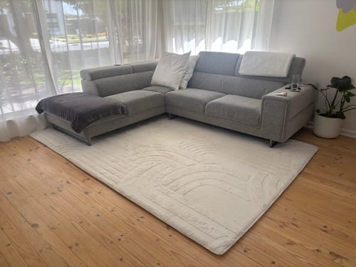 A customer's Vanilla Cream Mellow Mat with a carved design, placed on a wooden floor in a living room in front of a sofa.